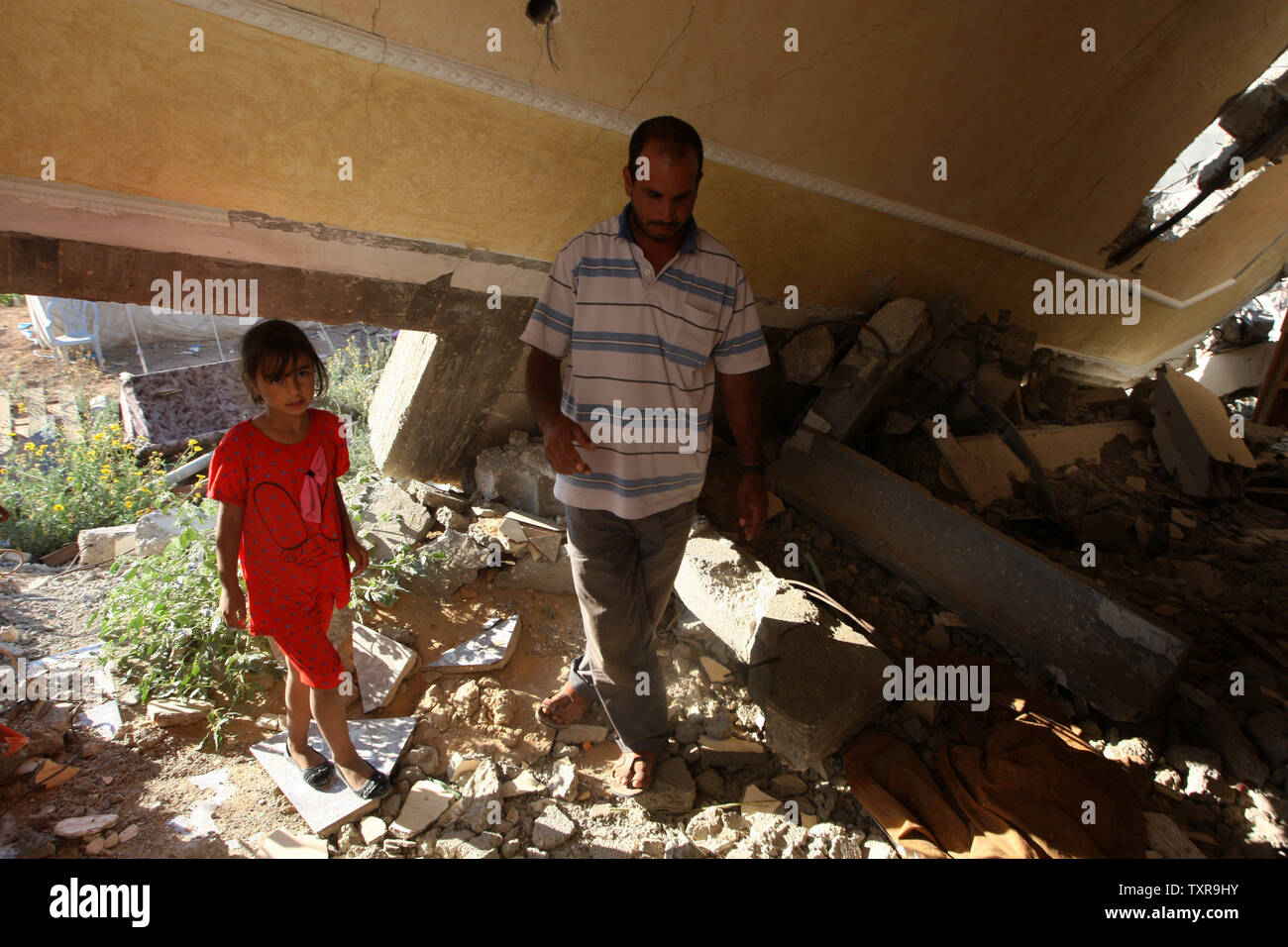 Hamada palestinese Qudeh cammina con sua figlia nella sua casa distrutta durante i 50 giorni di guerra tra Israele e Hamas a Gaza durante l'estate del 2014, nel villaggio di Khuzaa, a est di Khan Yunis, nel sud della striscia di Gaza il 10 luglio 2015. La guerra ha avuto un pesante tributo a Gaza, uccidendo 2,251 palestinesi compresi più di 500 bambini, mentre 73 sono stati uccisi sul lato israeliano, compresi 67 soldati. Foto di Ismael Mohamad/UPI Foto Stock