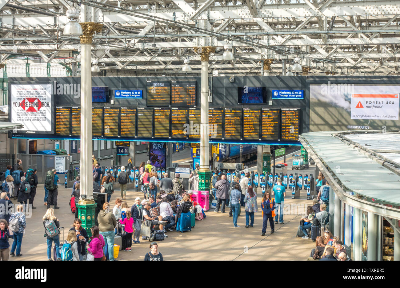 Scena in interni di un occupato la stazione ferroviaria Waverley di Edimburgo, con la luce del sole lo streaming attraverso il vetro e il tetto di travi. La Scozia, Regno Unito. Foto Stock