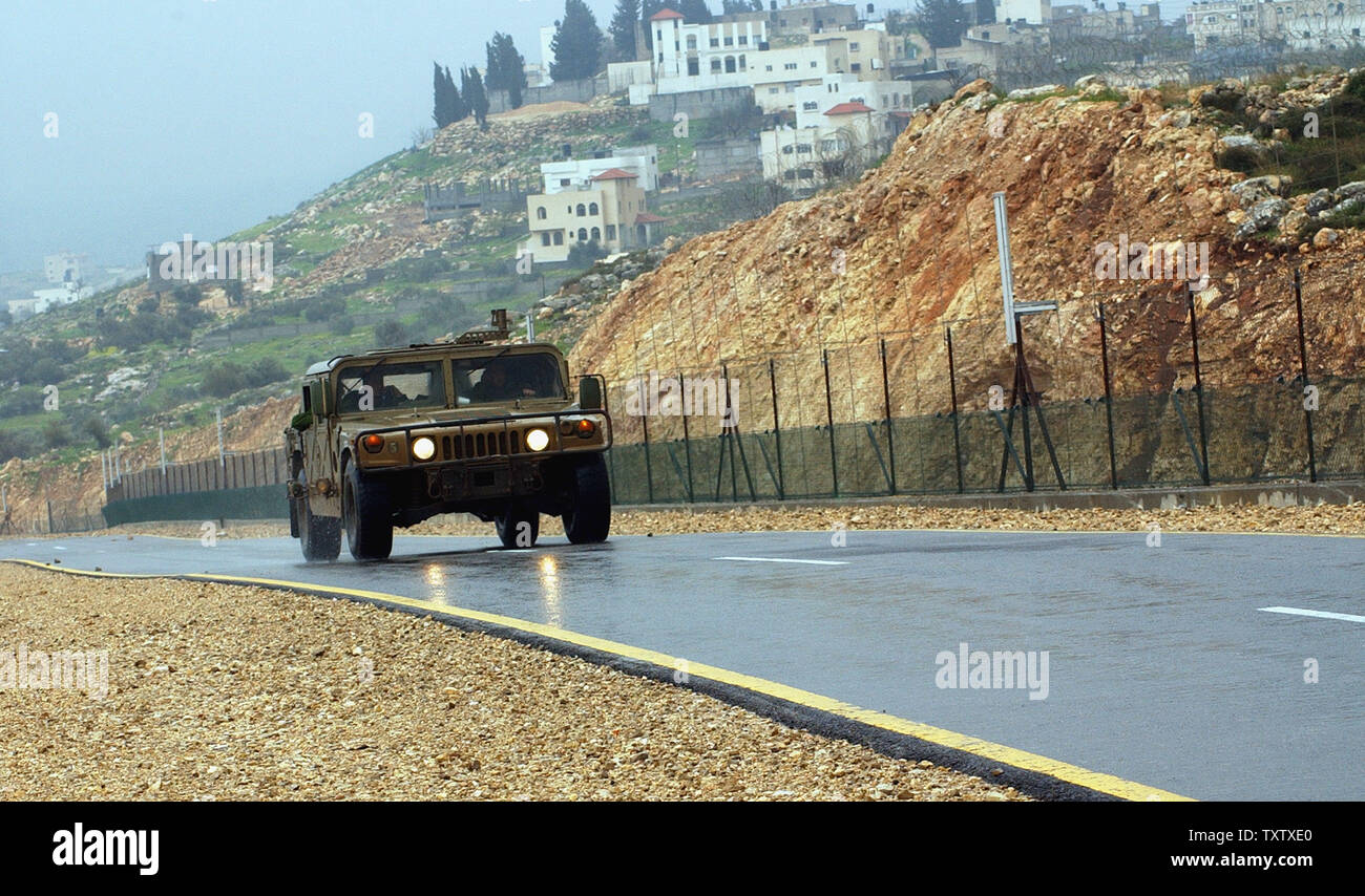 Un esercito israeliano humvee pattuglie di sicurezza la strada mediante la separazione israeliano recinto vicino al villaggio palestinese di Jayyous nella West Bank, il 19 febbraio 2004. (UPI foto/Debbie Hill) Foto Stock