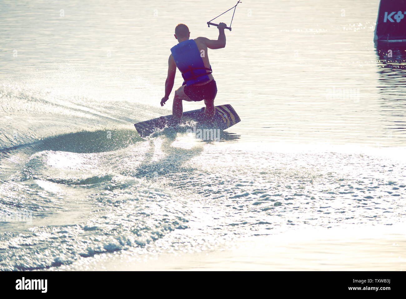 Surfer wakeboarding un Ollie salto al tramonto dorato. Esperto wakeboarder facendo Ollie jump, spruzzi di gocce di acqua nella fotocamera. Giovane uomo che cavalca c Foto Stock
