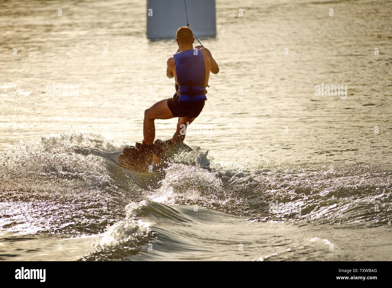 Surfer wakeboarding un Ollie salto al tramonto dorato. Esperto wakeboarder facendo Ollie jump, spruzzi di gocce di acqua nella fotocamera. Giovane uomo che cavalca c Foto Stock