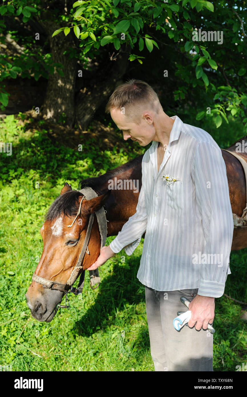 L uomo è in piedi accanto a un cavallo e accarezzare la sua testa. Foto Stock