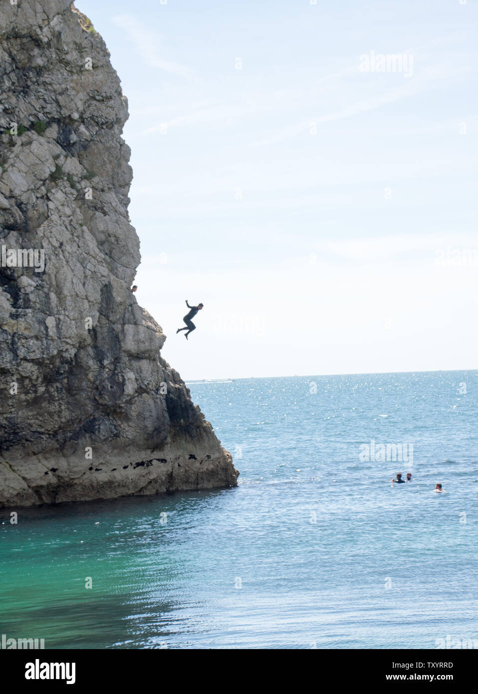 Uomo salta fuori da una scogliera in mare per battere il calore alla porta di Durdle Foto Stock
