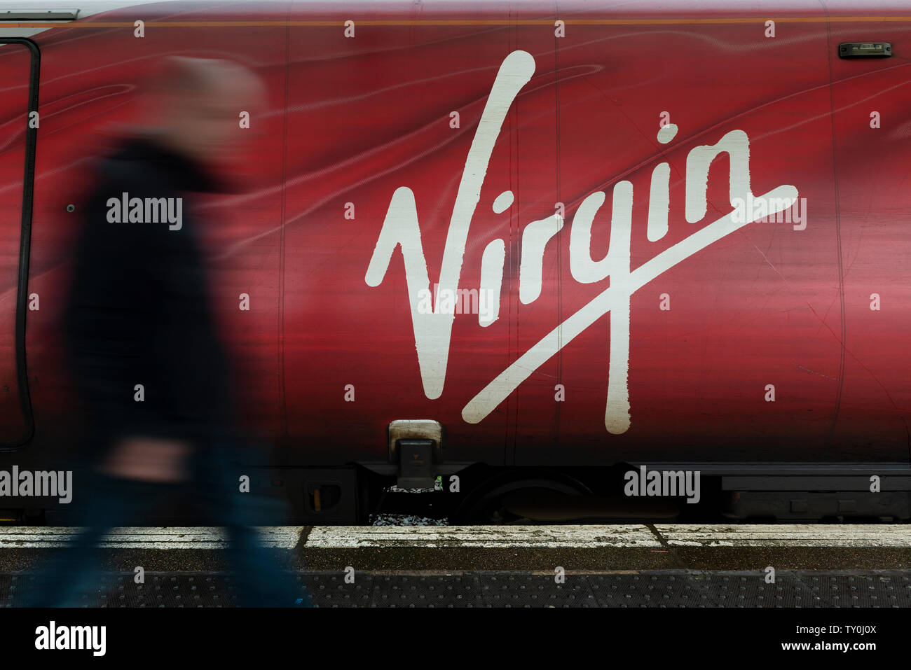 Un uomo cammina oltre il logo vergine come visto dal lato di una delle società di treni pendolino. Foto Stock