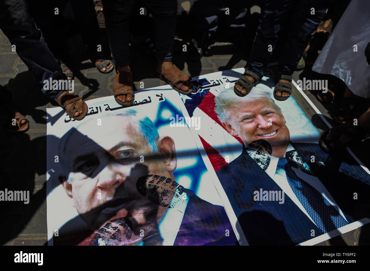 La striscia di Gaza, la Palestina. Il 25 giugno, 2019. Dimostranti palestinesi passo su un Poster raffigurante U.S. Presidente Donald Trump e il Primo Ministro israeliano Benjamin Netanyahu durante la protesta contro il Bahrain officina per noi di piano di pace nella Striscia di Gaza. Credito: SOPA Immagini limitata/Alamy Live News Foto Stock