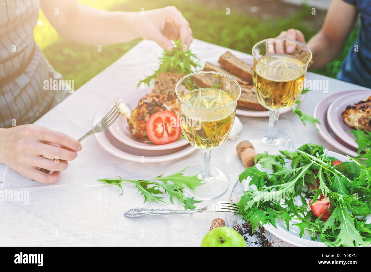 La cena in giardino. La gente mangia a tavola con vino e grigliate di pesce, verdure fresche e erbe aromatiche. Inquadratura orizzontale Foto Stock