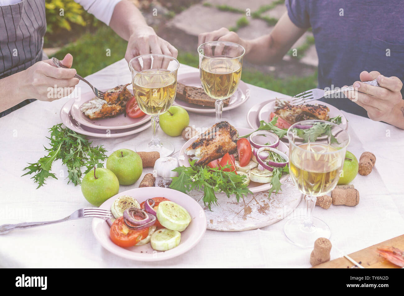 La cena in giardino. La gente mangia a tavola con vino e grigliate di pesce, verdure fresche e erbe aromatiche. Inquadratura orizzontale Foto Stock