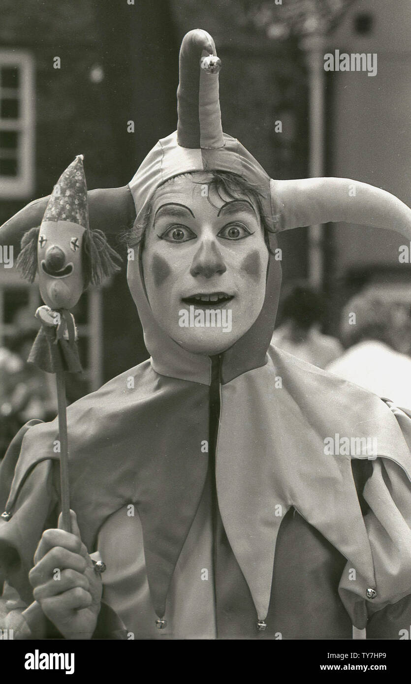 Anni ottanta, un ritratto di close-up di un moderno-giorno jester o intrattenitore vestito in un costume che richiamano le loro controparti storiche, Inghilterra, Regno Unito. In epoca medievale, un buffone era un esecutore itinerante che ha intrattenuto la gente comune in occasione di fiere e mercati, mentre il 'buffone di corte" è stato un membro della famiglia reale il cui lavoro era di divertire il re e i suoi ospiti a banchetti e feste. Giullari hanno una lunga storia e sono stati descritti in molti di Shakespeare's gioca, inclusi "Twelfth Night', dove Feste il giullare è descritto come "abbastanza saggi da riprodurre lo stolto". Foto Stock