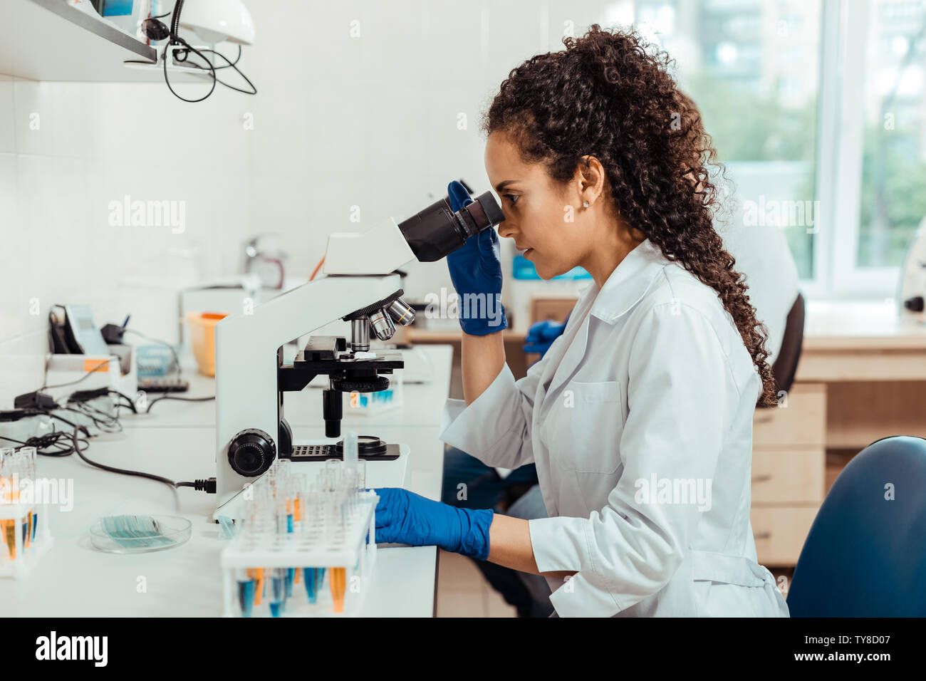 Smart giovane donna seduta di fronte al microscopio Foto Stock