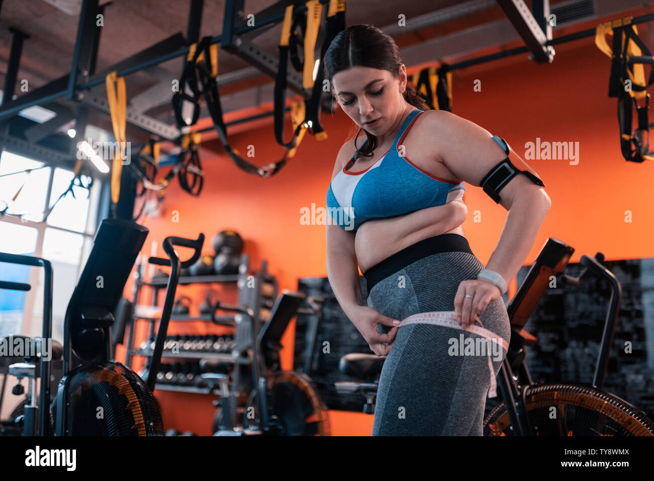Paffuto donna in grigio leggings misurando le cosce prima di allenamento Foto Stock