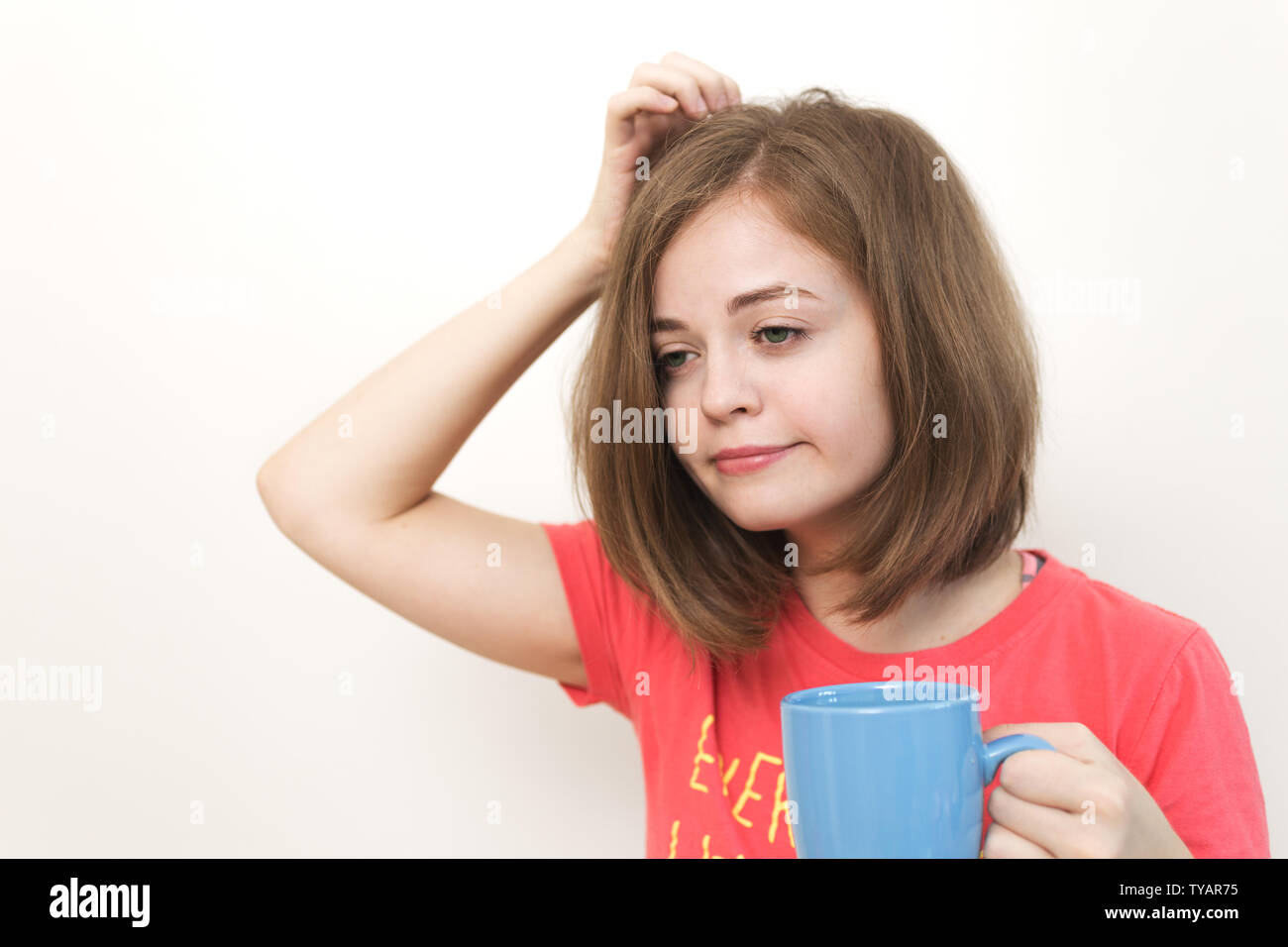 Ritratto di giovane donna caucasica girl, sbadigli, stanchezza e sonnolenza con cespuglioso capelli disheveled tenendo una tazza di caffè Foto Stock