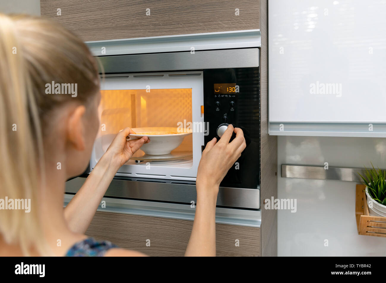 Donna riscaldare il cibo nel forno a microonde a casa Foto Stock