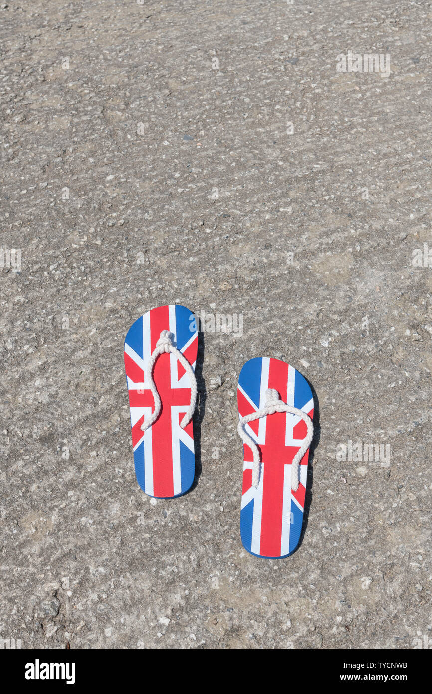 Union Jack flip-flop su pavimentazione in cemento - metafora 2021 UK staycation, vacanze a casa, staycation Cornwall, staycation break, flip flop calzature. Foto Stock