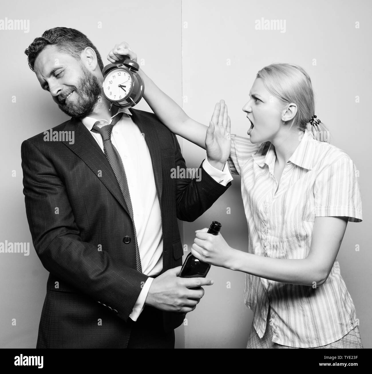 Dipendenza alcolismo o abuso di alcool. L uomo che soffre di alcolismo. Arrabbiato moglie incontro ubriaco marito tardi a casa. Imprenditore con bottiglia di alcool e la donna con la sveglia. Cosa oclock è. Foto Stock