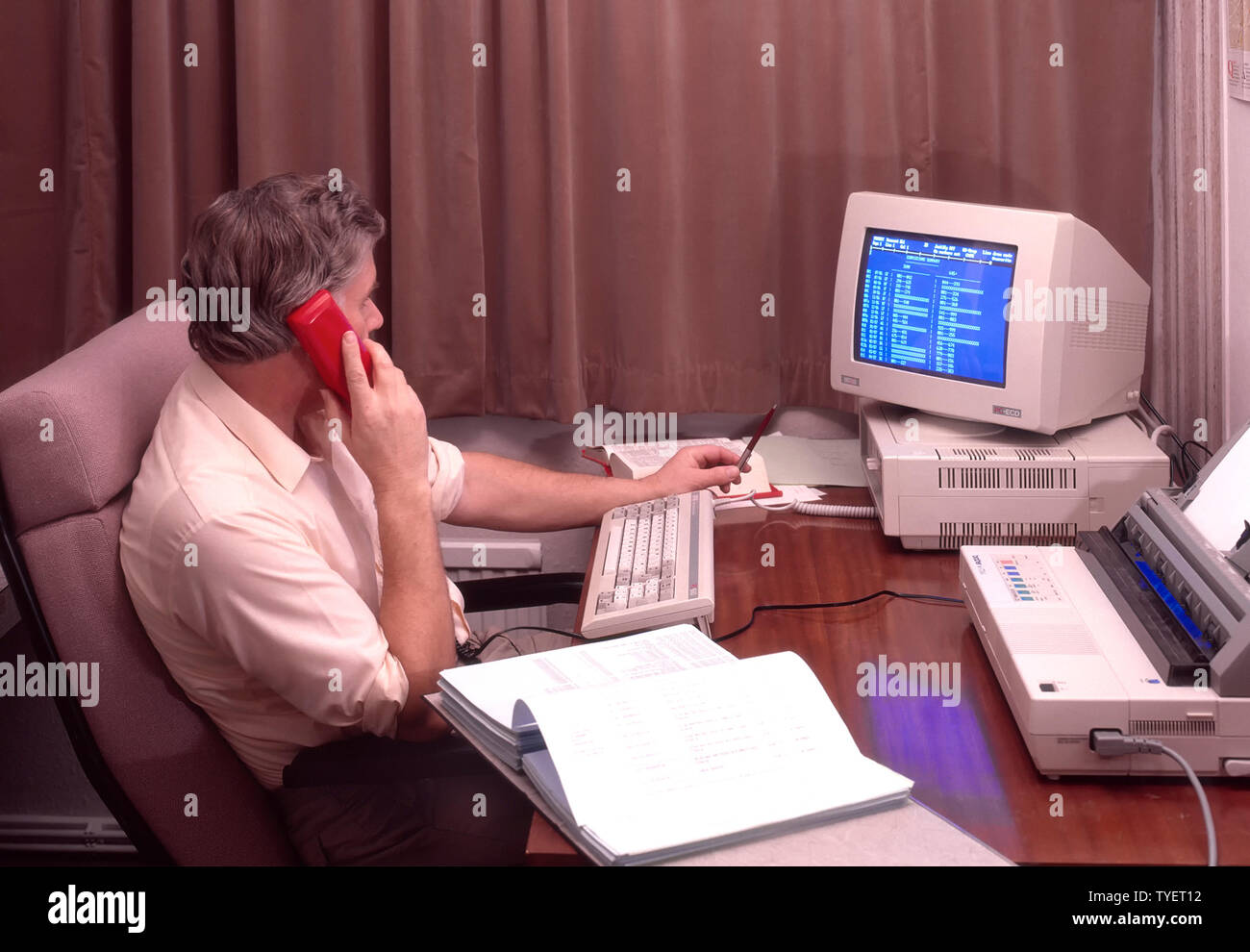 Immagine d'archivio storica del 1988 uomo d'ufficio, lavoratore indipendente, seduto alla scrivania, che lavorava fino a tardi da casa, tende chiuse con telefono fisso rosso, computer desktop Amstrad, schermo blu e archivio stampante anni '1980 nel modo in cui eravamo WFH in Inghilterra nel Regno Unito negli anni '80 Foto Stock