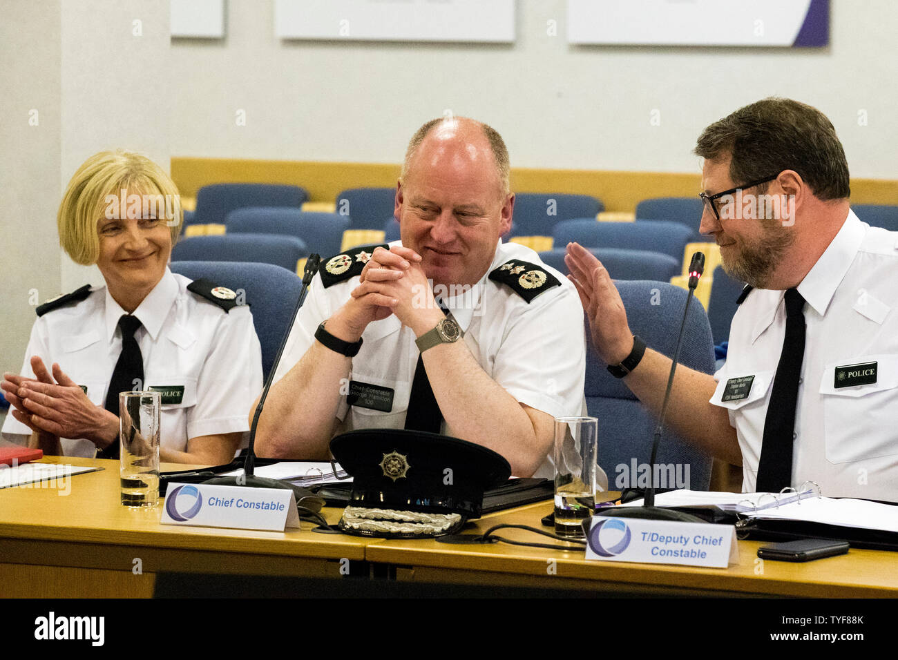 PSNI in uscita CHIEF CONSTABLE Sir George Hamilton (centro) si diedero dei colpetti leggeri sul retro dalla temporanea Deputy Chief Constable Stephen Martin (a destra) e applaudito dalle T/Assistant CHIEF CONSTABLE Barbara grigio durante il suo incontro finale della Northern Ireland Policing Board a Belfast. Foto Stock