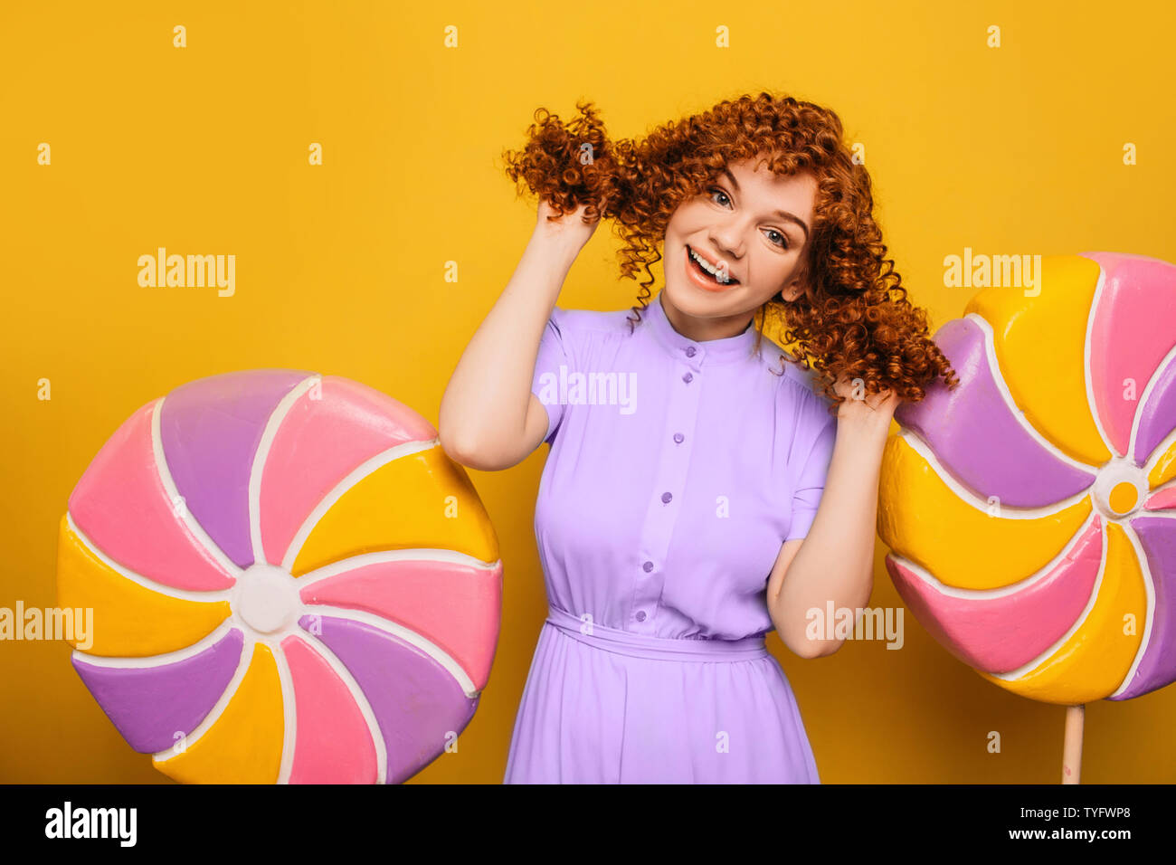 Ricci i capelli rossi donna positiva avente divertimento su lecca lecca sfondo. Sì mi piace dolce caramelle Foto Stock