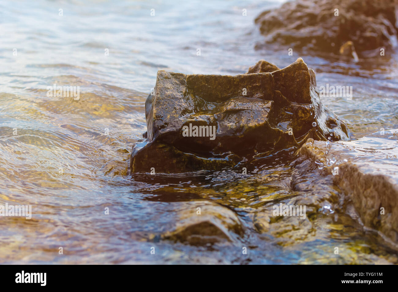 La pietra vicino al fiume. Onde eseguire sul litorale. Tramonto d'estate. I raggi del sole si riflettono nell'acqua Foto Stock