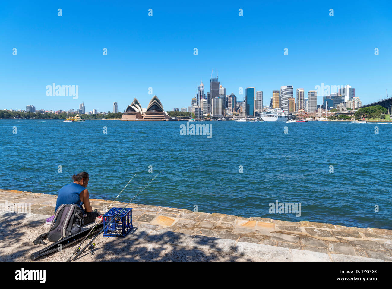 Il pescatore pesca dal lungomare di Kirribilli davanti al quartiere centrale degli affari e la Opera House di Sydney, Nuovo Galles del Sud, Australia Foto Stock