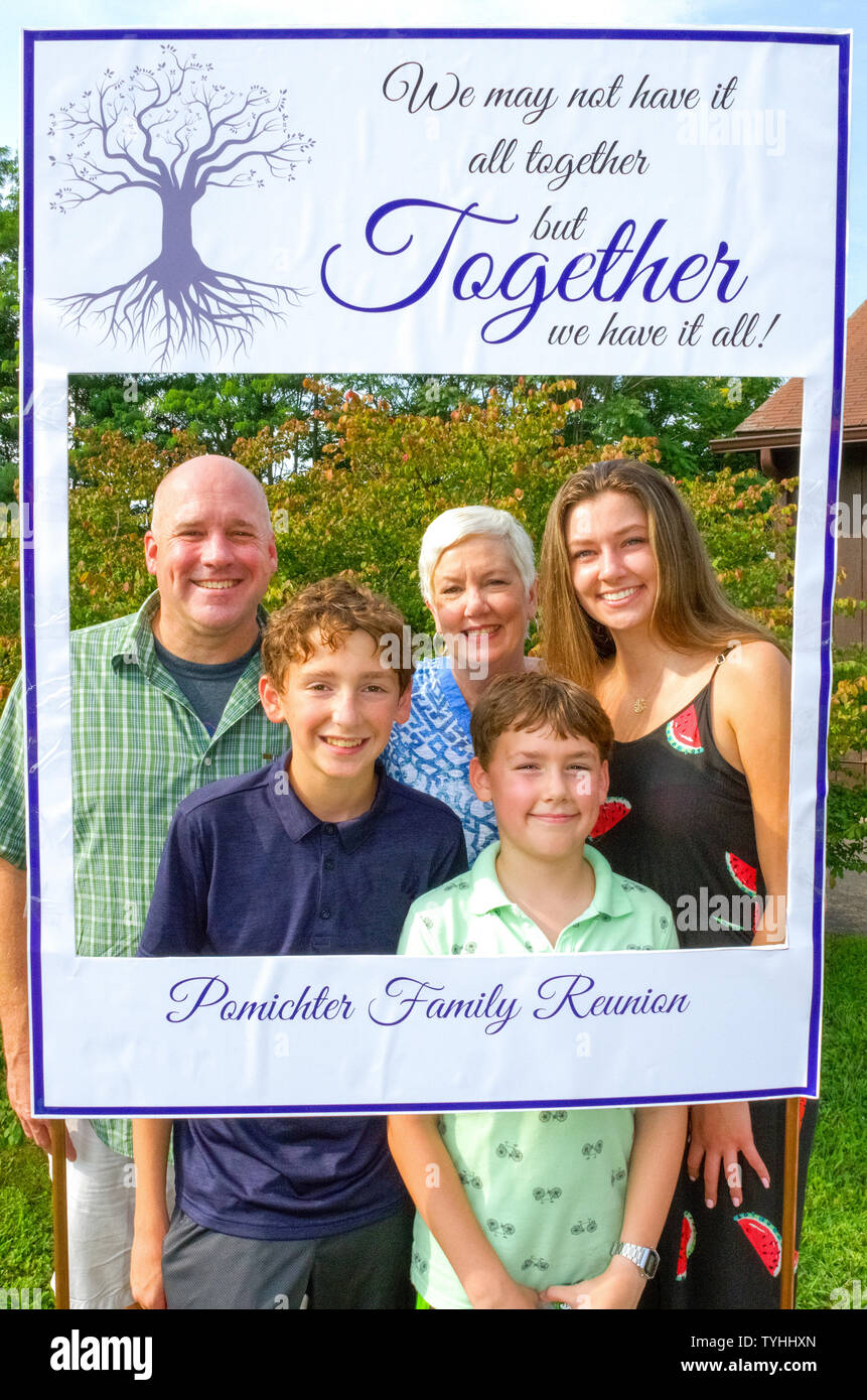 Tre generazioni pongono in un sapiente cut-out photo frame per un ritratto di famiglia in un American Family Reunion in un giorno di estate in Connecticut, Stati Uniti d'America. I partecipanti più anziani ad una tipica famiglia reunion sono generalmente i nonni, genitori, fratelli e cugini prima, mentre i più giovani potrebbe essere la seconda, la terza o la quarta cugini. Alcune riunioni familiari sono tenuti su una normale base annuale, o possono essere le occasioni speciali ogni quinto o decimo anno o così. È sempre un tempo di incontrare i membri più recenti della famiglia estesa e di condividere storie, fotografie e cibo. Foto Stock