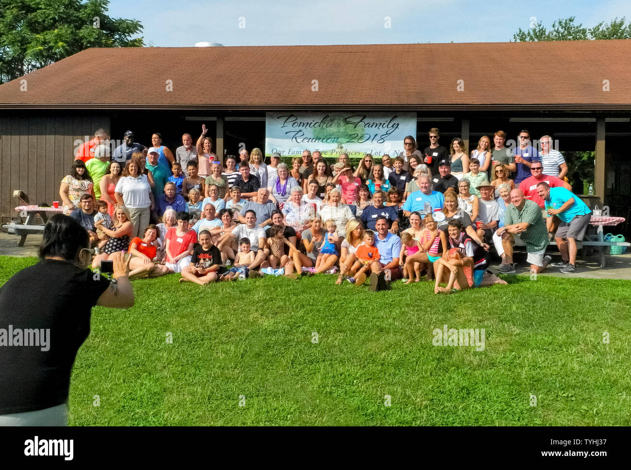 Adulti e bambini di molti secoli posano per una foto di gruppo durante un grande American Family Reunion su una soleggiata giornata estiva nel Connecticut, Stati Uniti d'America. I partecipanti più anziani ad una tipica famiglia reunion sono generalmente i nonni, genitori, fratelli e cugini prima, mentre i più giovani potrebbe essere la seconda, la terza o la quarta cugini. Alcune riunioni familiari sono tenuti su una normale base annuale, o possono essere le occasioni speciali ogni quinto o decimo anno o così. È sempre un tempo di incontrare i membri più recenti della famiglia estesa e di condividere storie, fotografie e cibo. Foto Stock