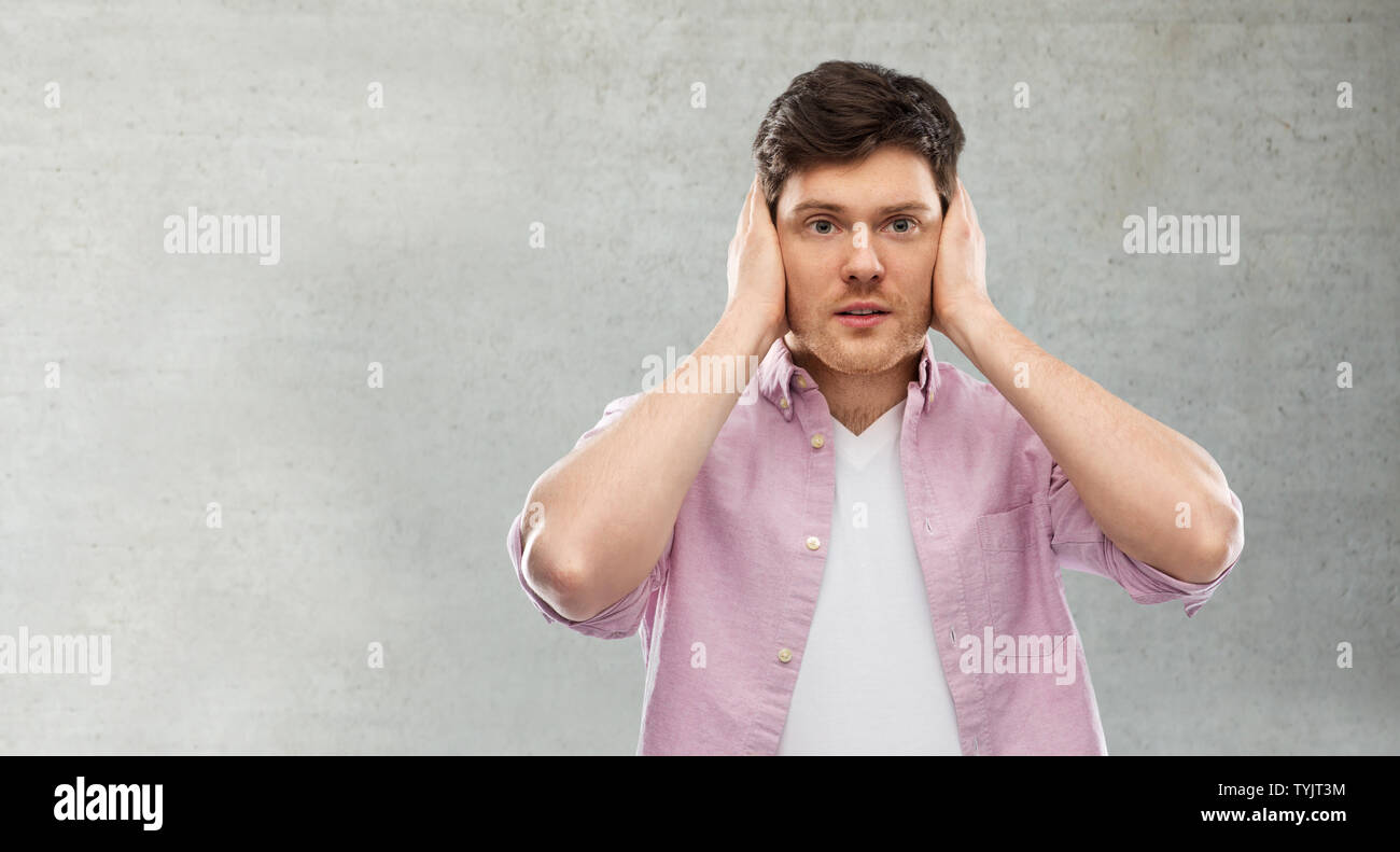 Uomo di chiudere le orecchie con le mani su grigio muro di cemento Foto Stock