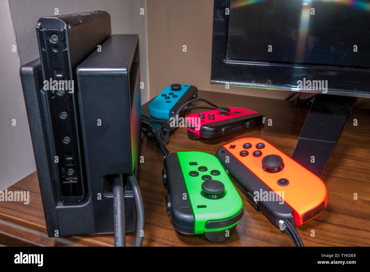 Quattro controller di gioco di vari colori luminosi, a fianco di un interruttore Nintendo console su un tavolo di legno. Foto Stock