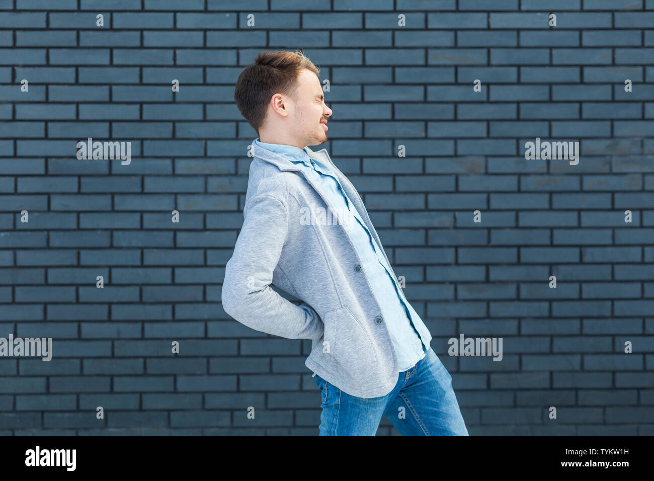 Indietro o dolore renale profilo vista laterale ritratto di malati o stanchi bel giovane biondo uomo in uno stile informale e permanente tenendo la sua dolorosa indietro. indoo Foto Stock