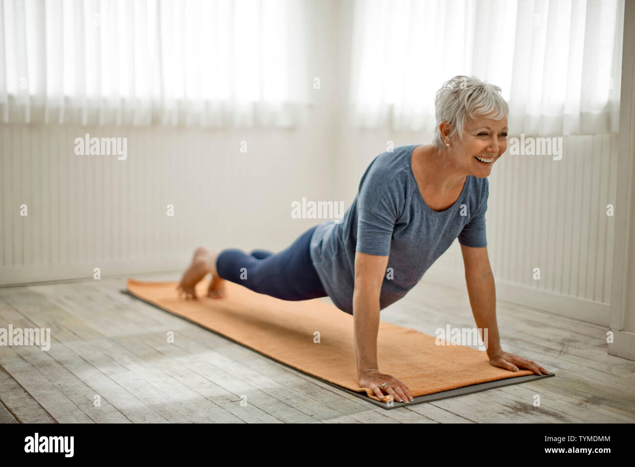 Donna matura sorride come fa un paio di push-up sul suo materassino yoga. Foto Stock