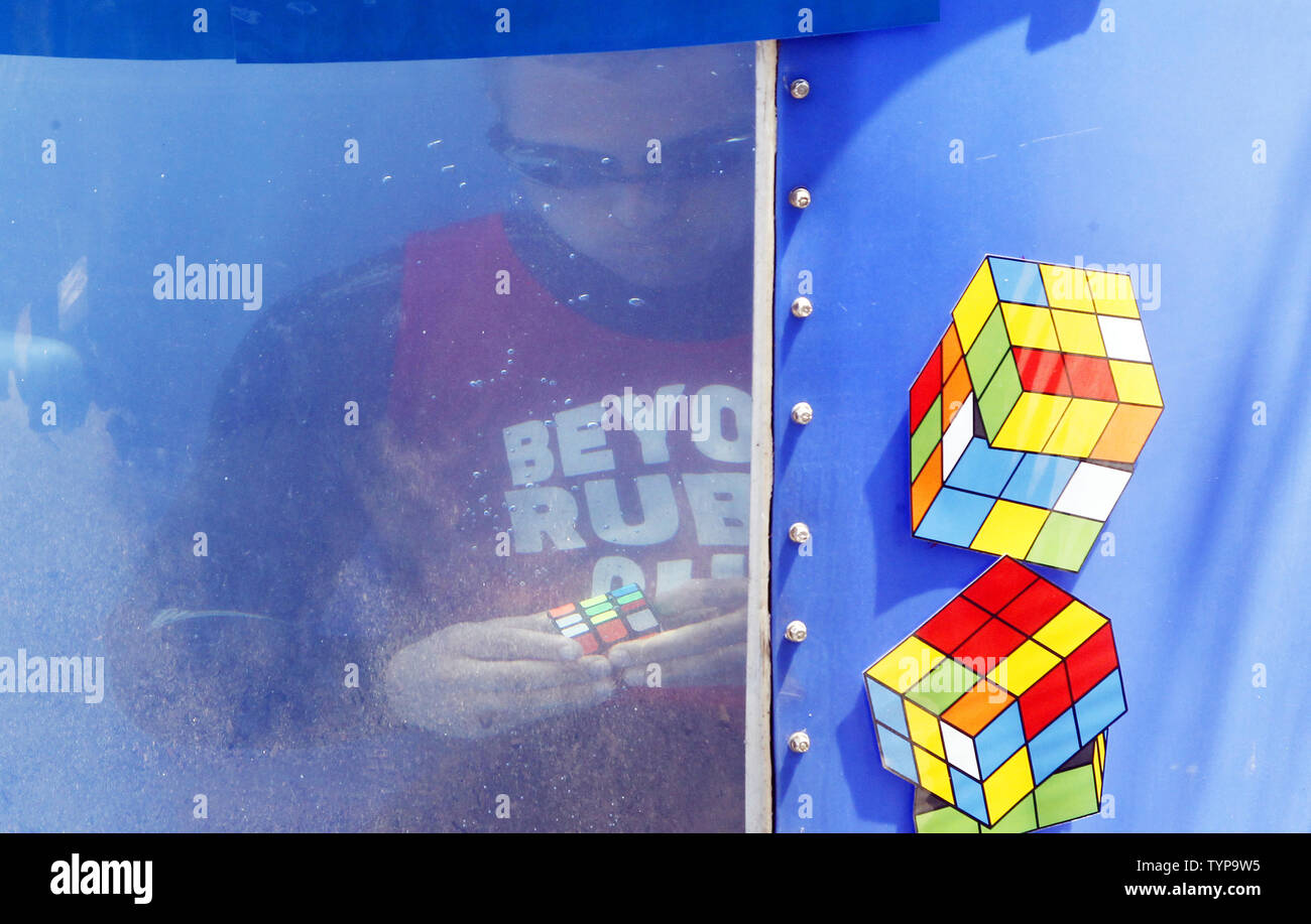 North American velocità campione del cubo di Anthony Brooks risolve un cubo di Rubik puzzle in un serbatoio di acqua come egli tenta di rompere i record Guinness per la maggior parte risolti cubetti sott'acqua in un respiro a livello nazionale il cubo di Rubik campionato al Liberty Science Center di Jersey City, NJ il 1 agosto 2014. Brooks impostare un nuovo record di risoluzione di 5 cubi in 1:18 battendo il vecchio record di registrazione di 4 cubi risolto in 1:30. UPI/John Angelillo Foto Stock