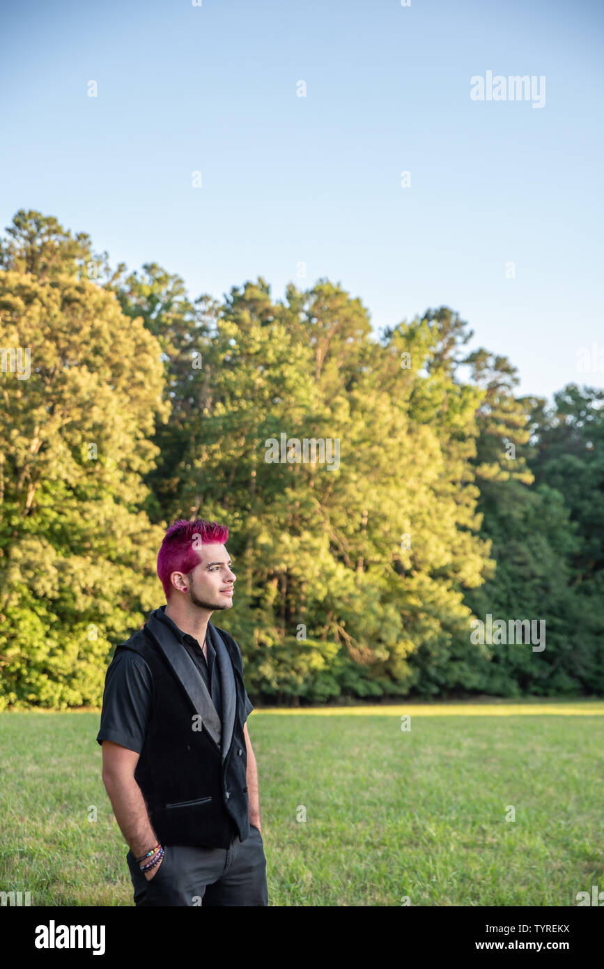 Bianco alternativa uomo caucasico con capelli rosa all'esterno guardando in lontananza, contemplativo. Alberi in background con vuoto vuoto lo spazio in camera per Foto Stock