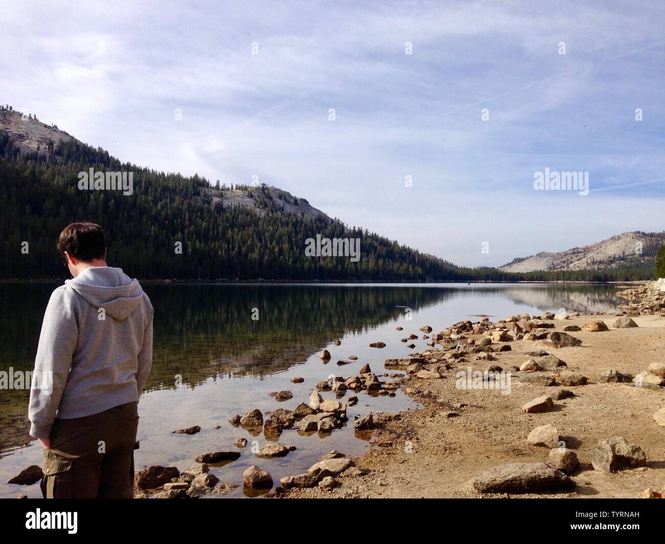 Man Standing perso in pensieri sul bordo di un lago vetroso Foto Stock
