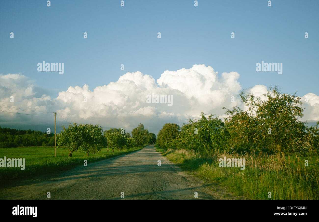 Strada in un villaggio in un campo il cielo blu e nuvole bianche contro l'orizzonte Foto Stock