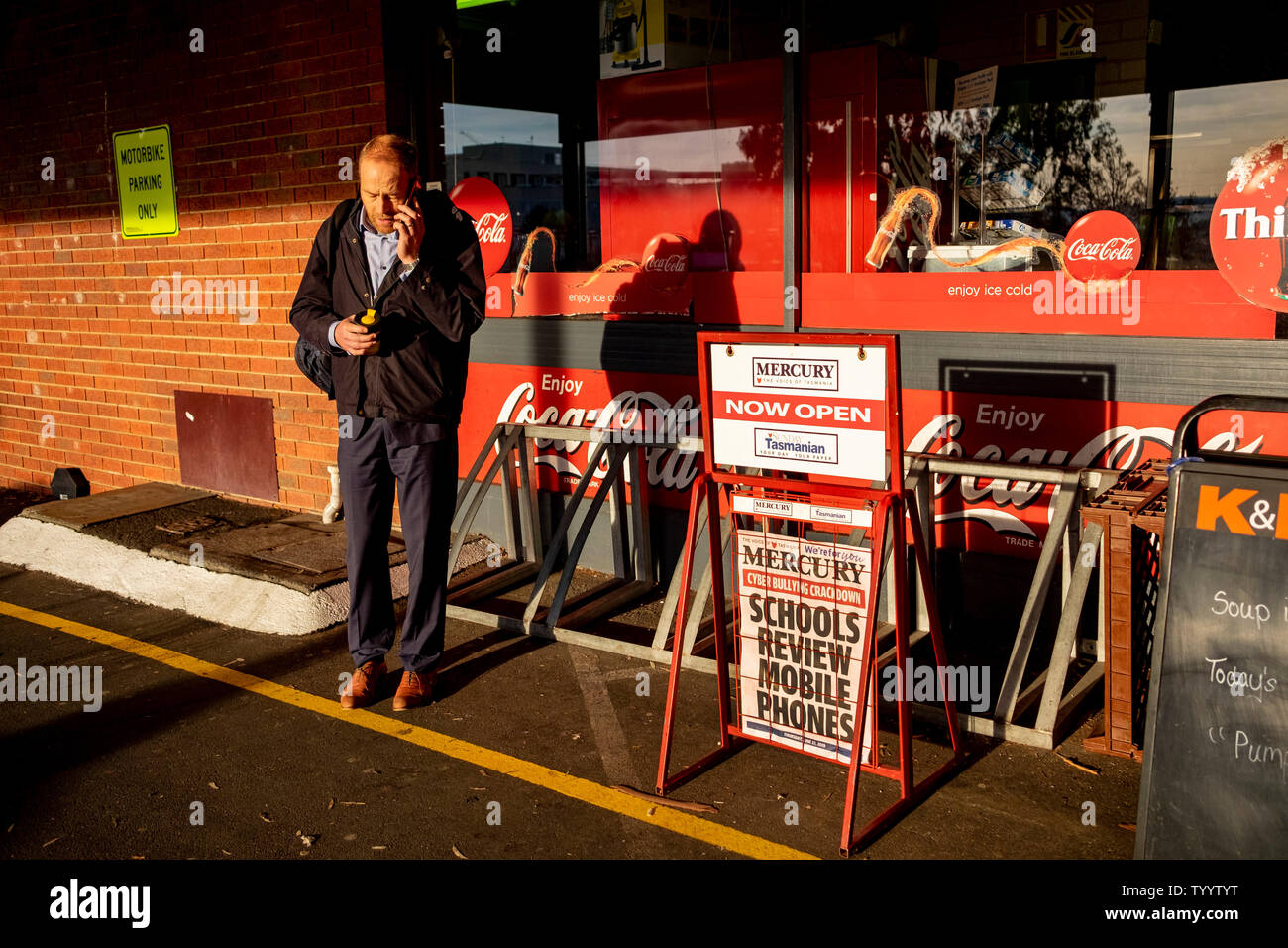 Un uomo con un telefono cellulare vicino a un banner di giornali annunciando divieto proposto sui telefoni cellulari nelle scuole australiane Foto Stock