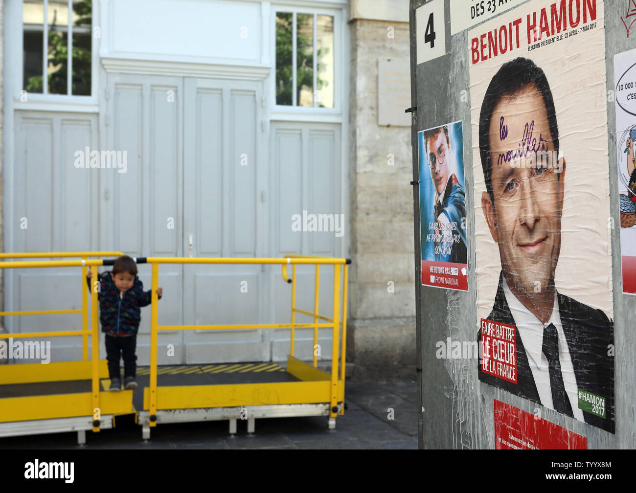 Un bambino gioca accanto a una campagna di manifesti del rightwing socialista elezioni presidenziali contender Benoit Hamon sul loro modo di esprimere il loro voto per il primo turno di votazione a Parigi il 23 aprile, 2017. Il voto è in corso nel primo round di un imprevedibile elezioni presidenziali il cui esito potrebbe rivelarsi cruciale per il futuro di un profondamente diviso il paese e un nervoso Unione europea. Foto di Maya Vidon-White/UPI Foto Stock