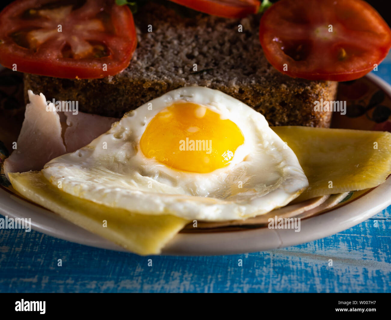 Uova a colazione, con pane senza glutine, formaggio, prosciutto e pomodoro, su un blu tavolo in legno Foto Stock