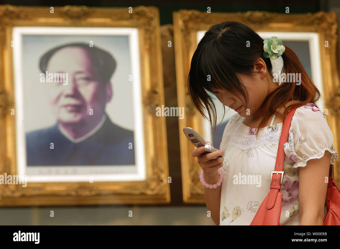 Una giovane ragazza cinese sorriso come lei legge un messaggio di testo sul suo telefono cellulare, nei pressi di un ritratto della Cina al fine timoniere Mao Zedong, nel centro di Pechino del 12 giugno 2006. Molto è cambiato in tutta la Cina poiché i giorni di Mao la rivoluzione culturale e il regime comunista. (UPI foto/Stephen rasoio) Foto Stock
