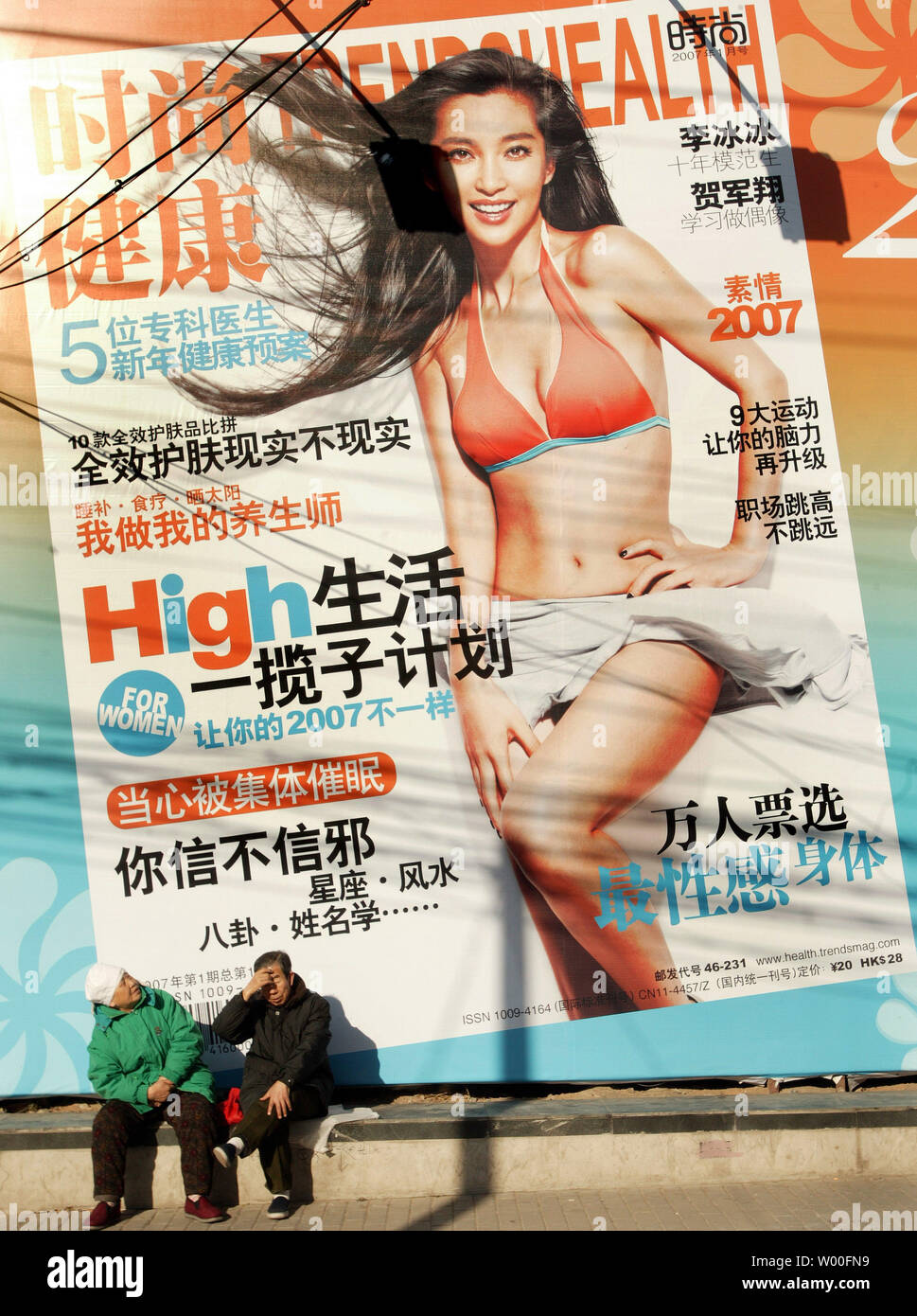 Una coppia di anziani si riscalda se stessi nel sole di mezzogiorno di fronte a un annuncio di un nuovo e moderno lifestyle magazine per le strade del centro di Pechino, Cina, il 21 gennaio 2007. Entro solo negli ultimi anni la Cina ha fatto di avere praticamente nessun "occidentale" stile riviste concentrandosi sulla salute, bellezza e stili di vita per ora vanta centinaia che sono venduti in tutto il paese. (UPI foto/Stephen rasoio) Foto Stock
