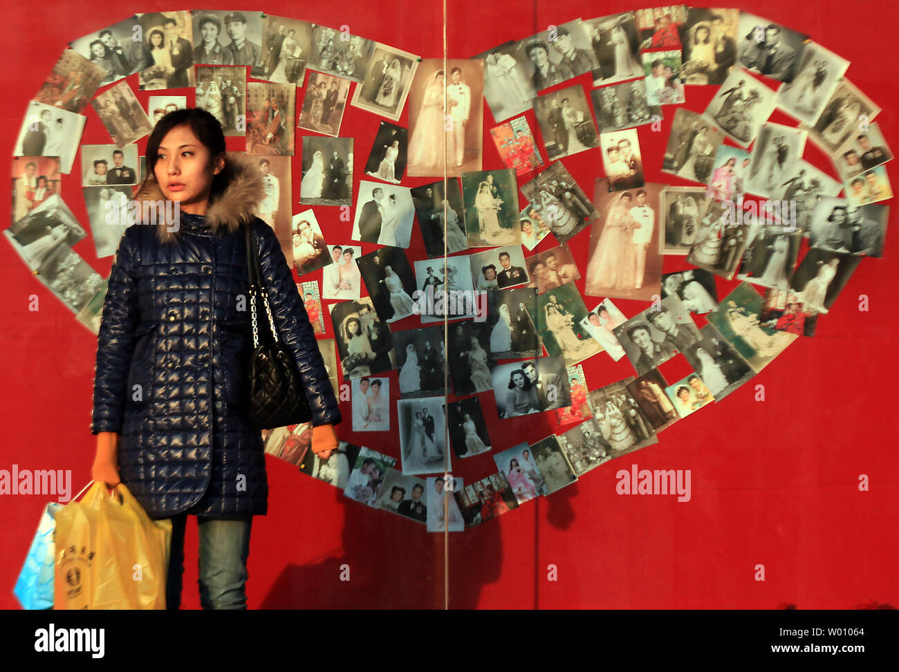 Una donna cinese sta in piedi di fronte ad un cuore decorativo fatto di matrimonio fotografie sulla vetrina di un centro commerciale a Pechino il 15 febbraio 2012. L'età media dei primi matrimoni in Cina La capitale è salito a 27, un anno di età superiore ai tre anni fa. Come scegliere il cinese a sposarsi più tardi nella vita, il tasso di divorzio ha girato fino in tutto il paese con la pressione di lavoro, più veloce moderni stili di vita e lo sviluppo economico della Cina contribuendo a rotto i matrimoni. UPI/Stephen rasoio Foto Stock