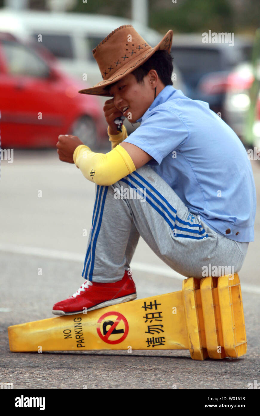 Un Cinese auto attendant siede su un no-cono di parcheggio nella città costiera di Qingdao, un importante porto nella parte orientale della provincia di Shandong, il 19 agosto 2014. Solo due decenni fa auto personali proprietà in Cina era inferiore al 15 percento, eppure è esplosa a oltre il 60 percento in soli dieci anni - esercitando forti pressioni su urbanisti per far fronte ad una domanda crescente di aree di parcheggio. UPI/Stephen rasoio Foto Stock