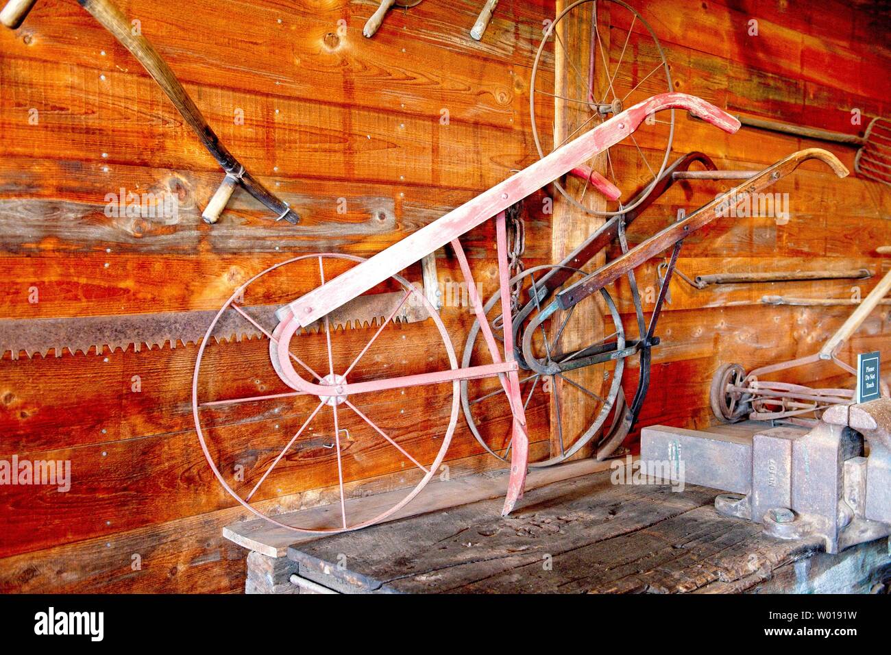 Un aratro antico siede su un tavolo in un fienile circondato da altri vecchi attrezzi agricoli Foto Stock