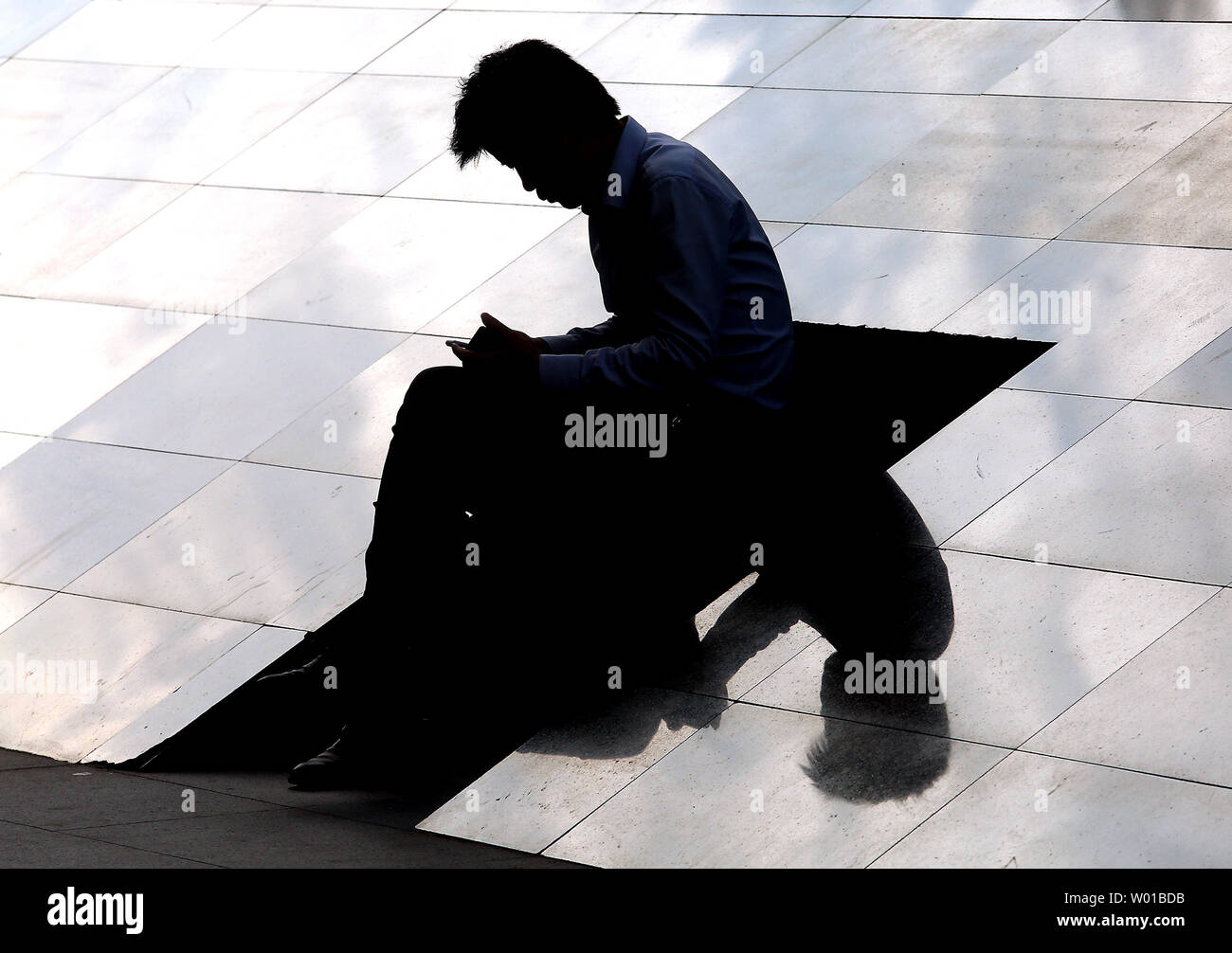 Un Cinese lavoratore di ufficio usa il suo smartphone al di fuori del suo ufficio durante la pausa per il pranzo a Pechino il 24 agosto 2016. Le incrinature sono cominciando a mostrare in Cina il mercato del lavoro come difficoltà commerciali e le imprese industriali sono entrambi di licenziare i dipendenti e il congelamento di nuove assunzioni. I dati del Ministero delle Risorse Umane e della sicurezza sociale indica la Cina del mercato del lavoro è costante, ma l'eccesso di offerta di manodopera e di carenze strutturali continuano a problemi dell'economia. Foto di Stefano rasoio/UPI Foto Stock