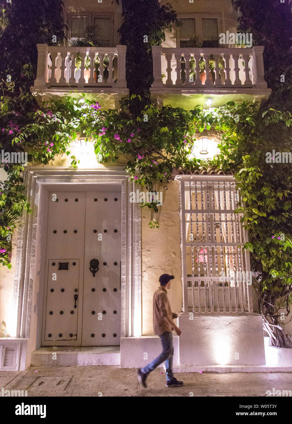 Un uomo cammina davanti a una storica e bella era coloniale edificio nel centro storico (Centro) di Cartagena, Colombia, con piante pendenti. Foto Stock