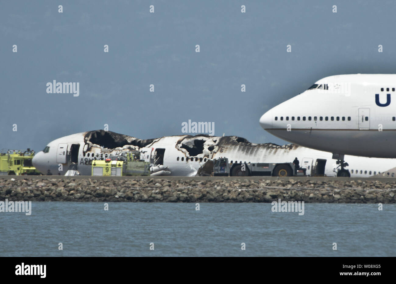 Un regno piano viene trainato passato i resti di un'Asiana Air Boeing 777 che si è schiantato in atterraggio sulla pista di San Francisco Aeroporto Internazionale di San Francisco il 6 luglio 2013. Il piano è stato proveniente da Seoul. UPI/Terry Schmitt Foto Stock
