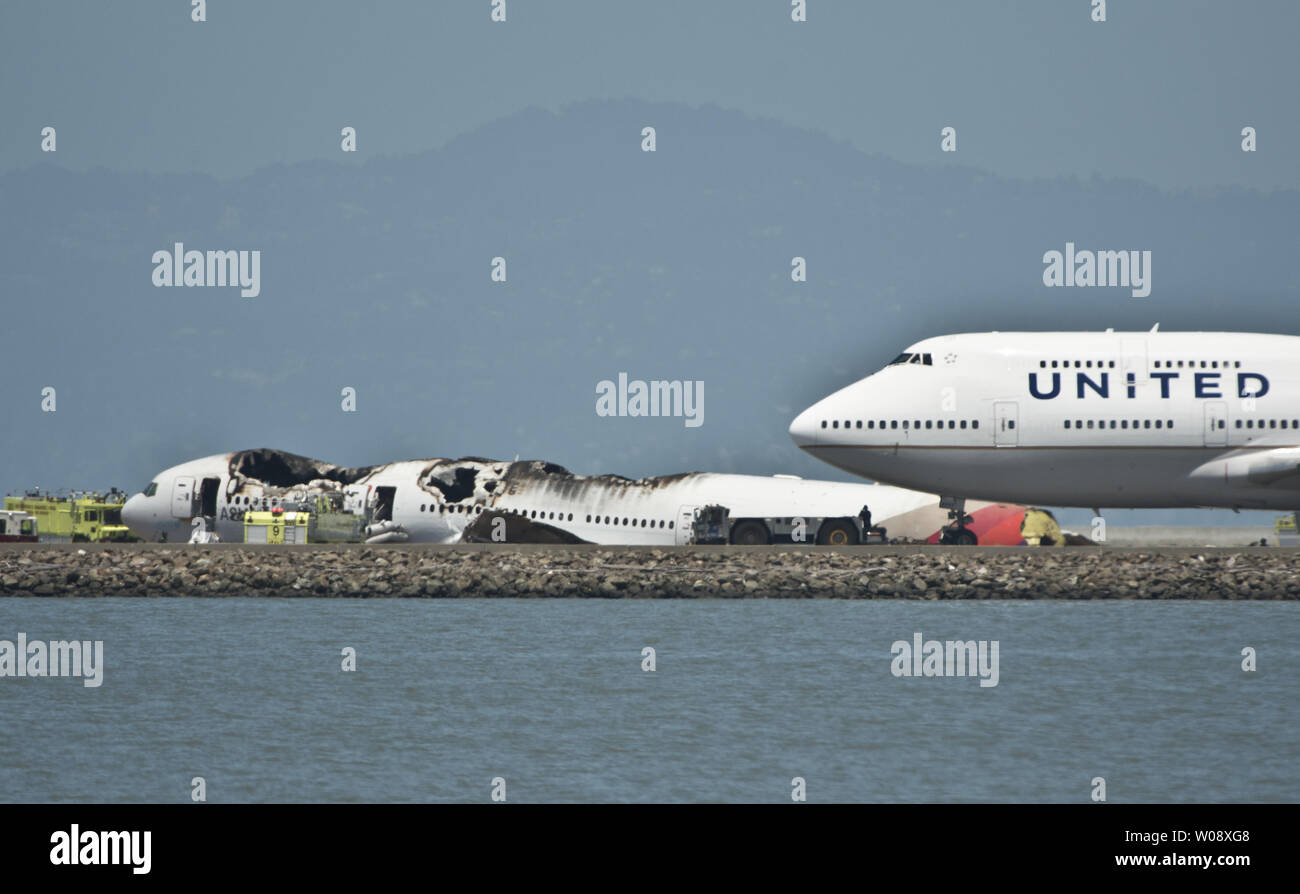 Un regno piano viene trainato passato i resti di un'Asiana Air Boeing 777 che si è schiantato in atterraggio sulla pista di San Francisco Aeroporto Internazionale di San Francisco il 6 luglio 2013. Il piano è stato proveniente da Seoul. UPI/Terry Schmitt Foto Stock
