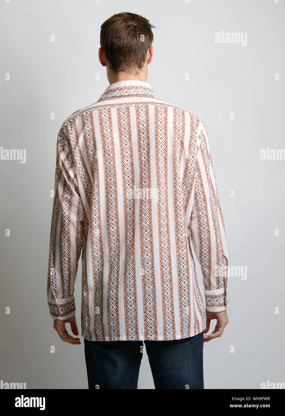 Un modello maschio caucasico di capelli marroni pone in una camicia a strisce vintage, la sua fotocamera rivolta verso la schiena, un editoriale di moda vintage maschile. Foto Stock