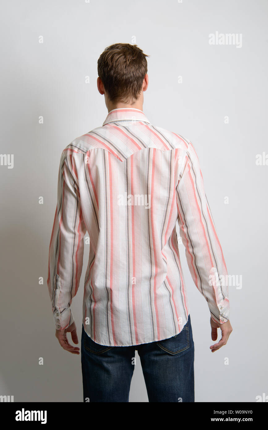 Un modello maschio caucasico di capelli marroni pone in una camicia a strisce vintage, la sua fotocamera rivolta verso la schiena, un editoriale di moda vintage maschile. Foto Stock