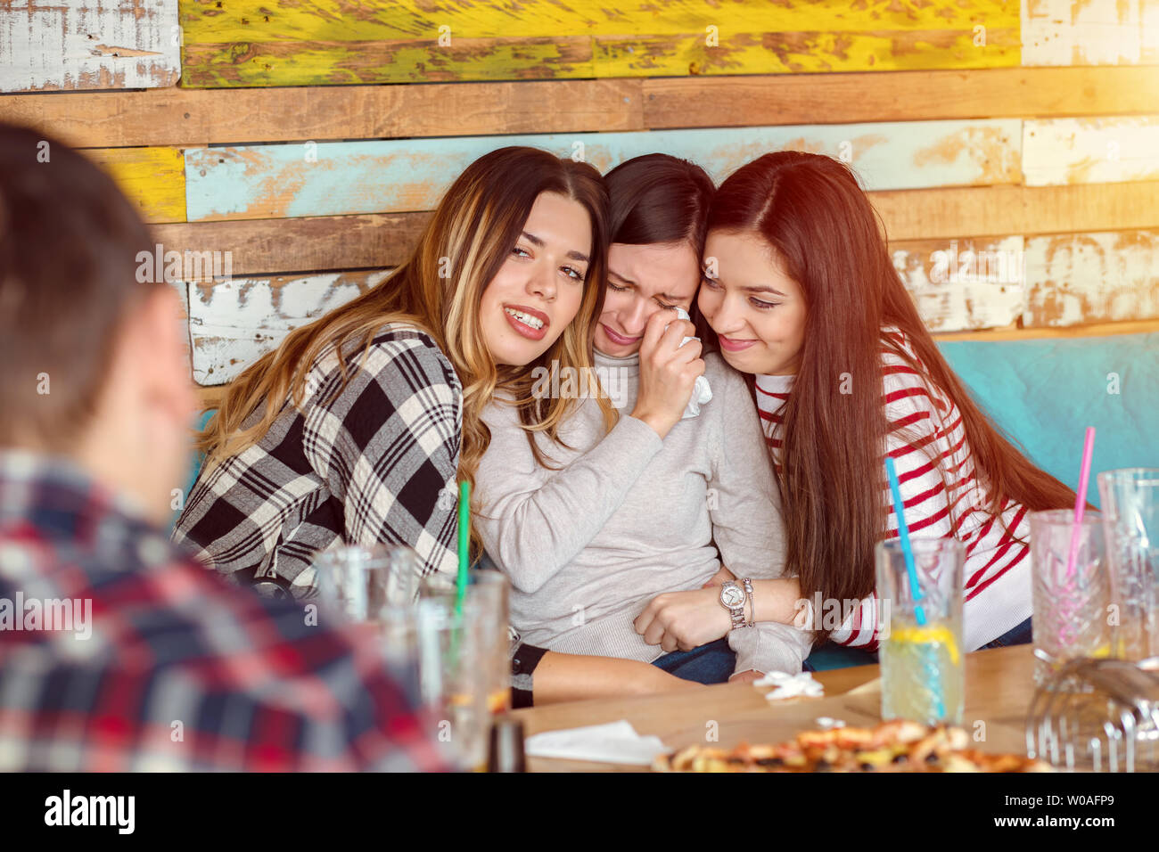 Gli amici di conforto e consolante il pianto giovane donna alla riunione di gruppo nel pub moderno Foto Stock