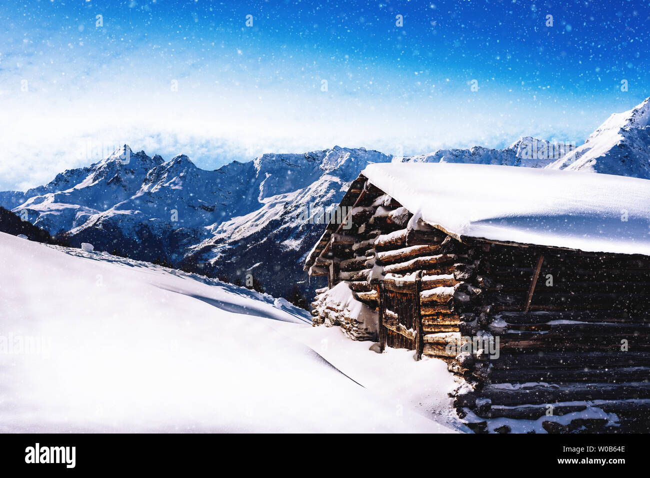 Alta altitudine chalet in legno cottage con luce di neve che cade con Alpi mountain range in background Foto Stock