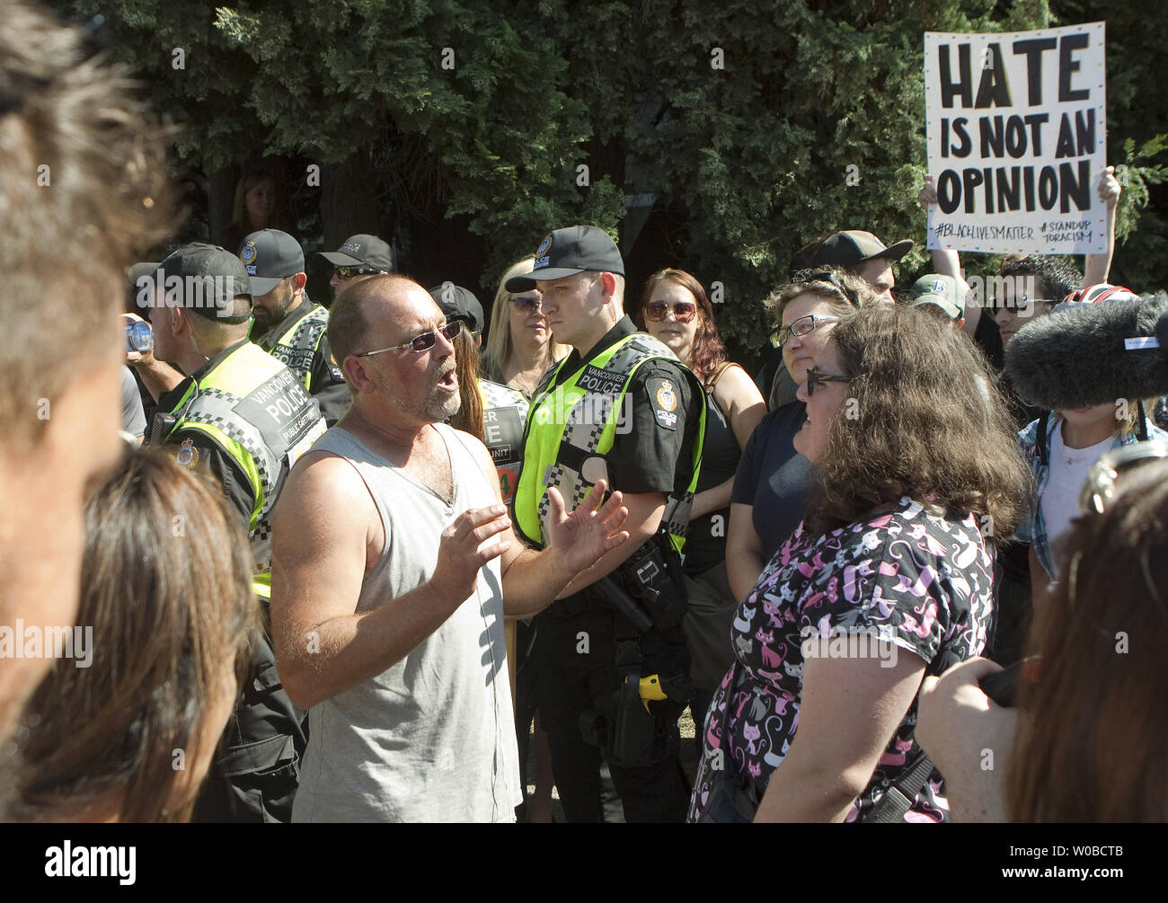 La polizia di Vancouver guarda un uomo dal lontano Rally destra dibattito con una donna, uno di migliaia di persone per protestare contro un piccolo di estrema destra al rally di Vancouver City Hall in Vancouver, Columbia Britannica il 19 agosto 2017. Estrema destra gruppi opporsi all Islam e del Canada alle politiche di immigrazione. Foto di Heinz Ruckemann/UPI Foto Stock